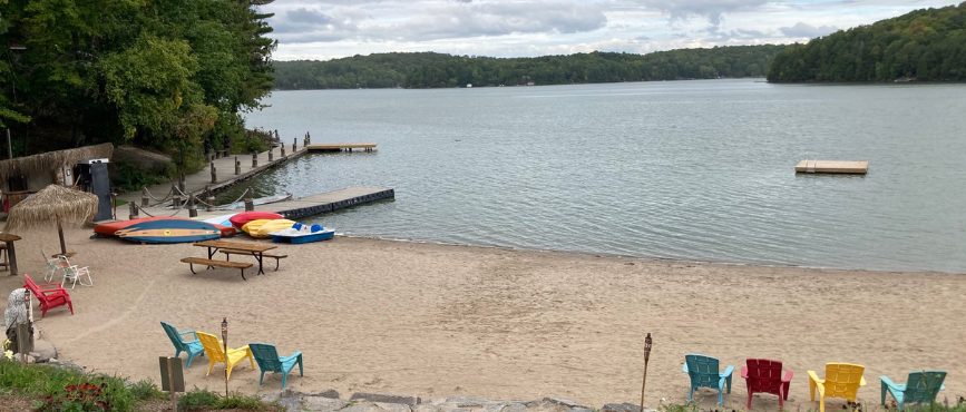 A beach on a lake with Muskoka chairs and canoes and a dock